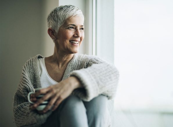 woman wearing a sweater enjoys a cup of tea by a windowsill