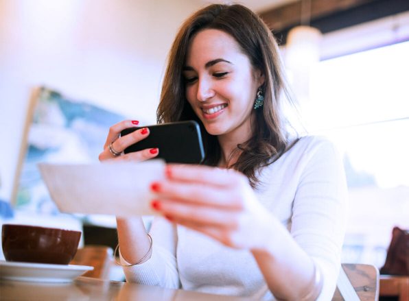 woman holding her mobile phone while taking a picture of a physical check