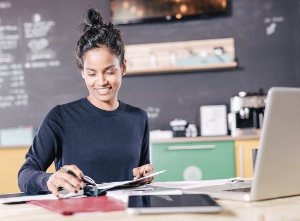 woman smiling at a desk while thumbing through a notebook